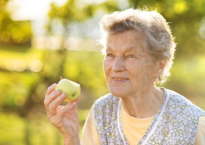 Senior lady in the sun holding an apple.