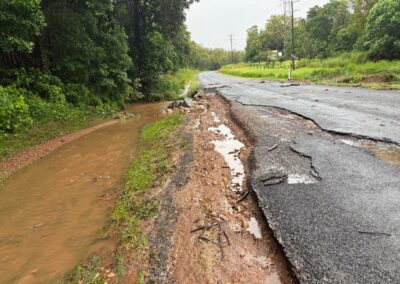 Roadside damage, with a chunk of the road washed away and lots of debris on the road.